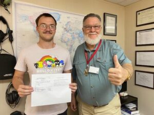 Two men posing with a document and smiling.