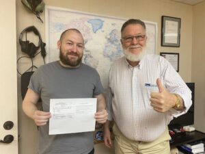 Two men holding a document, smiling together.